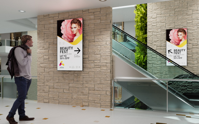 a man walks by two digital signage displays alongside an escalator in a shopping mall.