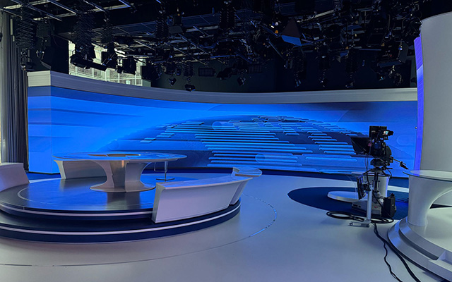 Ein TV-Studio mit Kamera und Pult vor einem gebogenen LED- Bildhintergrund.